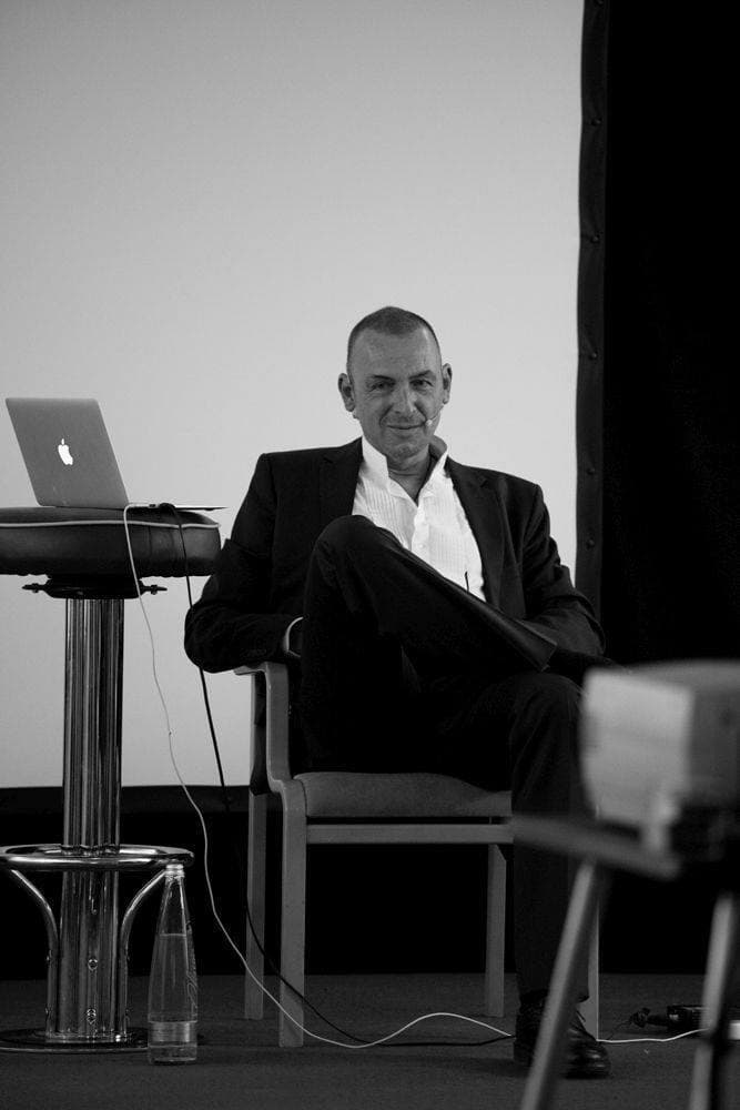 Orlando Owen seated on stage beside a laptop during a talk